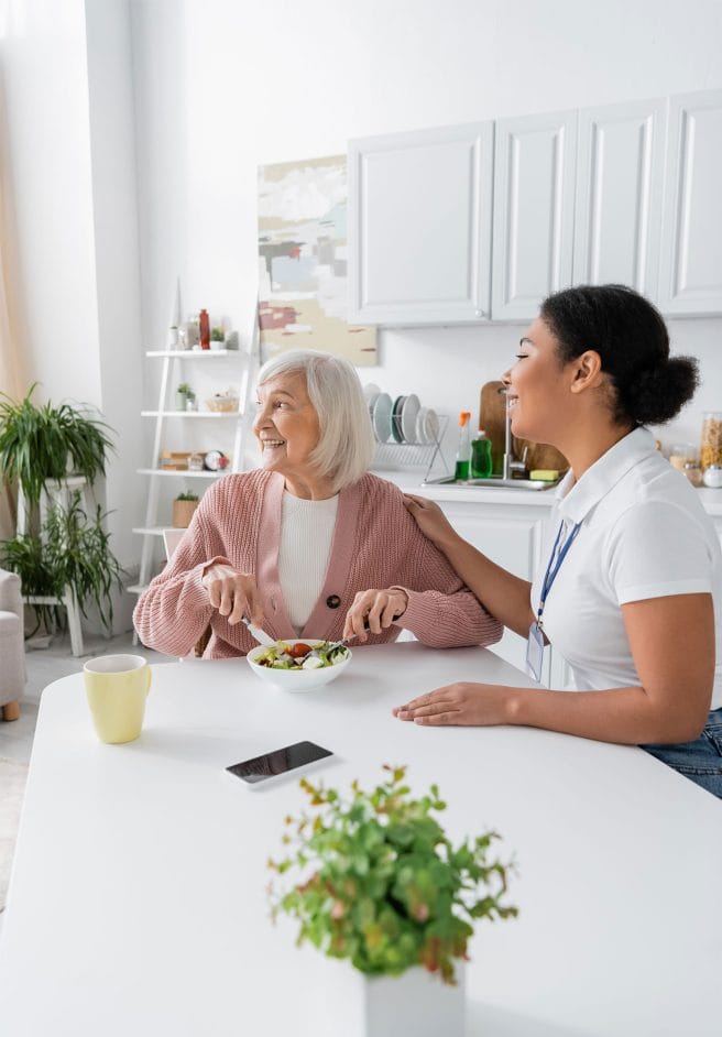 A care worker chatting with an older woman over a meal at home