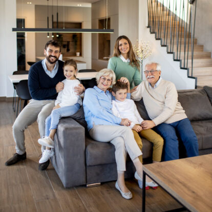 A happy multi-generational family relaxing together on a sofa in their bright living room, reflecting the commitment to work in partnership with people using the service and their families.