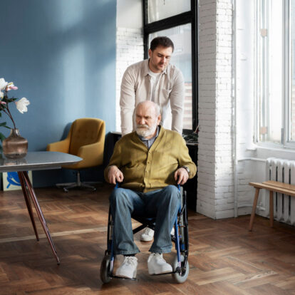A male support worker assisting an older man in a wheelchair to navigate smoothly through his living area, ensuring a safe home environment.